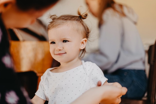 Ragazza graziosa sorridente felice che si tiene per mano donna che guarda i suoi occhi mentre si siede nella stanza contro qualcuno che suona il pianoforte