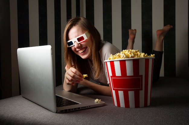 ragazza guardando uno spettacolo televisivo di notte in un computer portatile e mangiando popcorn