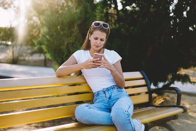 Ragazza hipster che invia messaggi di testo e controlla le notifiche sullo smartphone mentre si riposa al parco