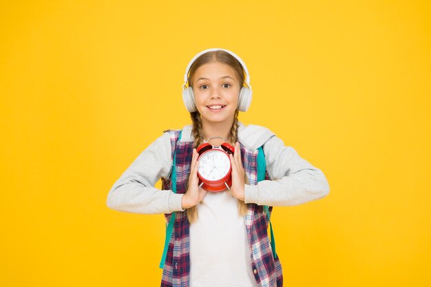 Ragazza hipster gestire il tempo correttamente studentessa stile casual tenere sveglia retrò periodo di educazione autunnale bambino ascoltare musica auricolari gestione del tempo nel concetto di scadenza esame infanzia