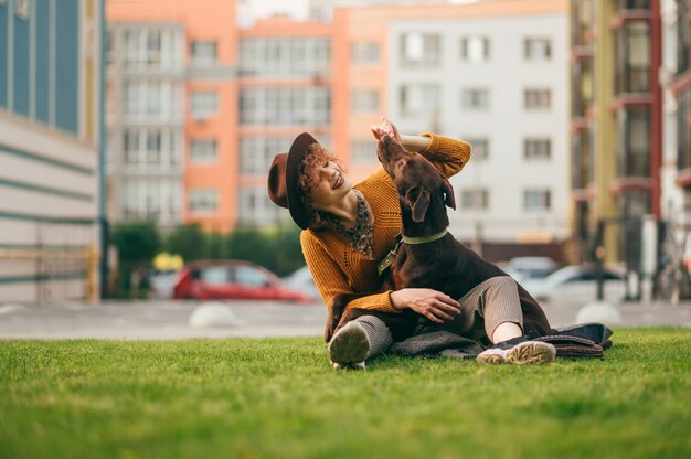 Ragazza in abiti alla moda e cappello si siede sul prato in cortile