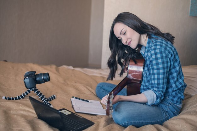 ragazza in abiti casual sul letto, registra blog di musica e suona la chitarra acustica