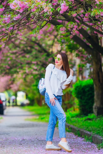 Ragazza in abiti eleganti e occhiali da vista tiene la mano tra i capelli molti fiori di ciliegio giapponesi