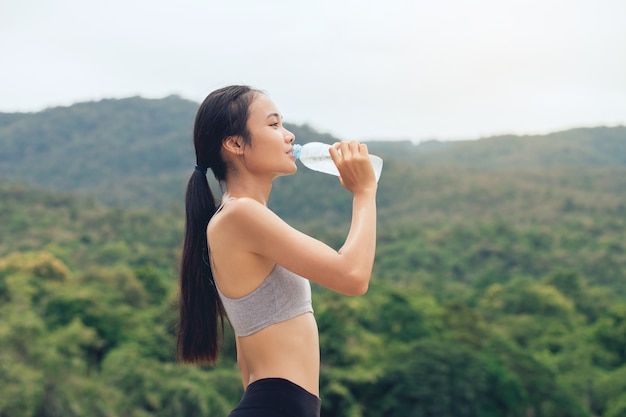 Ragazza in abiti sportivi beve l'acqua dalla bottiglia di plastica riciclata nel parco all'aperto dopo l'allenamento