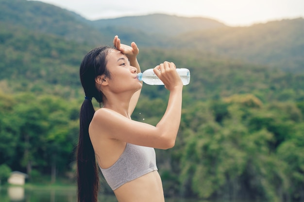 Ragazza in abiti sportivi beve l'acqua dalla bottiglia di plastica riciclata nel parco all'aperto dopo l'allenamento