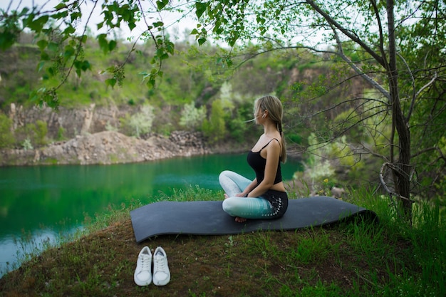 Ragazza in abiti sportivi medita vicino al lago