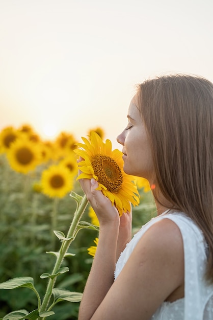 Ragazza in abito bianco che sente l'odore di un fiore di girasole.