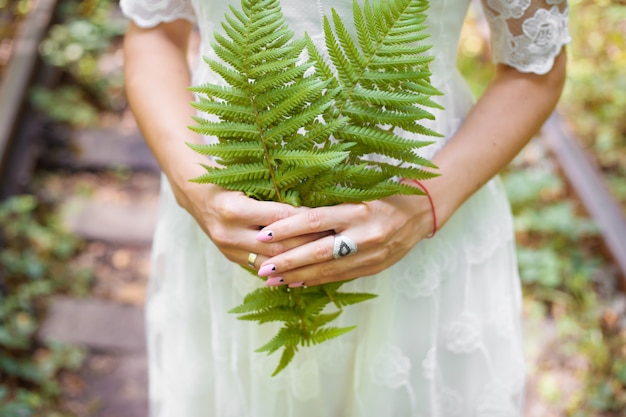 Ragazza in abito bianco, con foglie di felce verde nella foresta