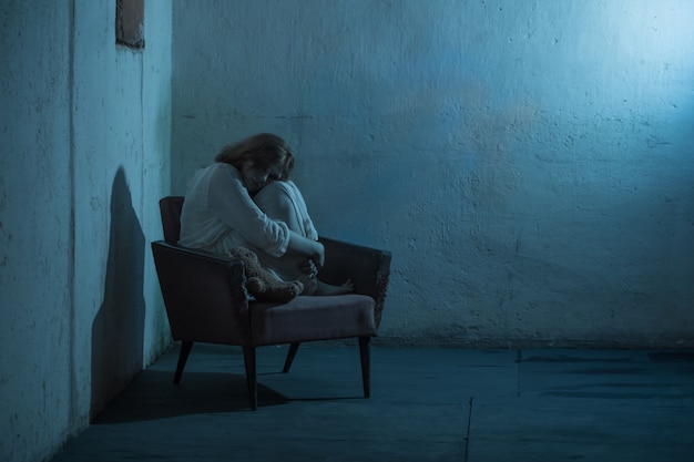 Ragazza in abito bianco sulla vecchia poltrona nel seminterrato