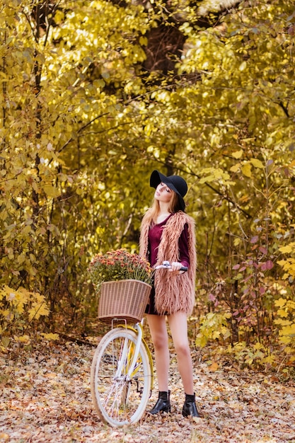 Ragazza in abito bordeaux e gilet con bici gialla in una passeggiata nel tardo autunno