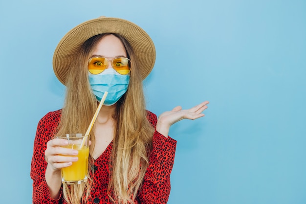 Ragazza in abito, cappello e occhiali da sole con una mascherina medica sul viso.