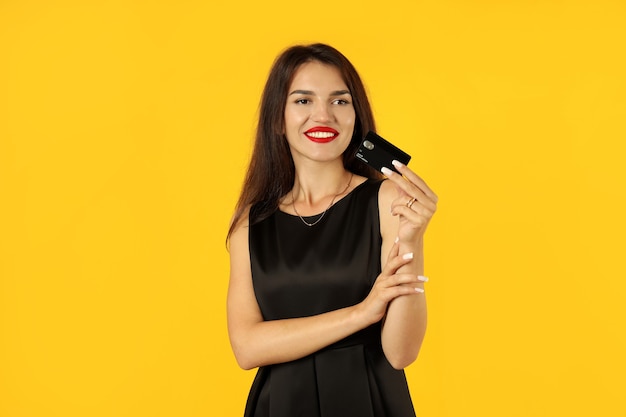 Ragazza in abito nero con carta di credito su sfondo giallo.