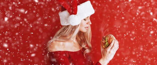 Ragazza in abito rosso e cappello da Babbo Natale con hamburger in mano