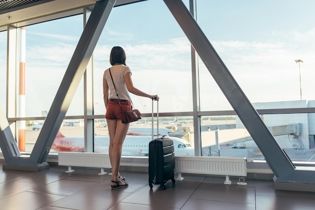 Ragazza in aeroporto vicino alle finestre del cancello sugli aerei sulla pista