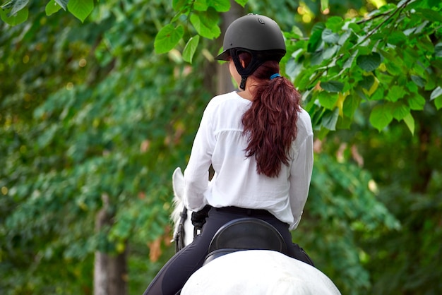 Ragazza in attrezzatura equestre che monta un cavallo vicino agli alberi