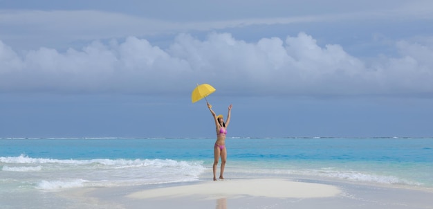 ragazza in bikini con un ombrello giallo sulla sabbia del mare