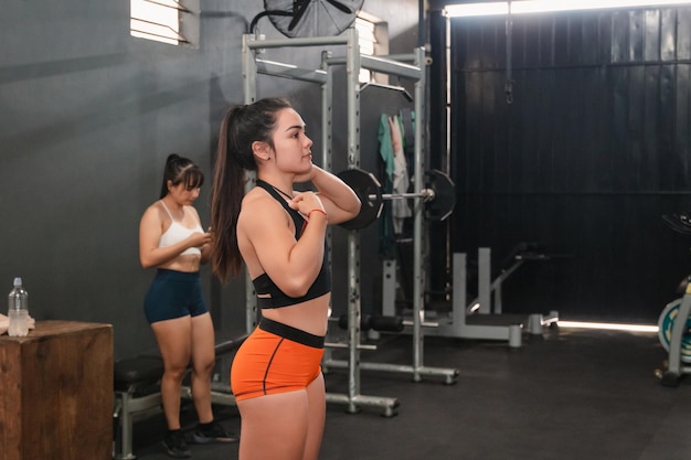 Ragazza in buona forma fisica che si prepara ad iniziare l'allenamento mentre il suo partner usa il cellulare in palestra