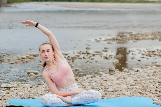 Ragazza in buona salute che si rilassa mentre medita e fa esercizio di yoga nella splendida natura sulla riva del fiume