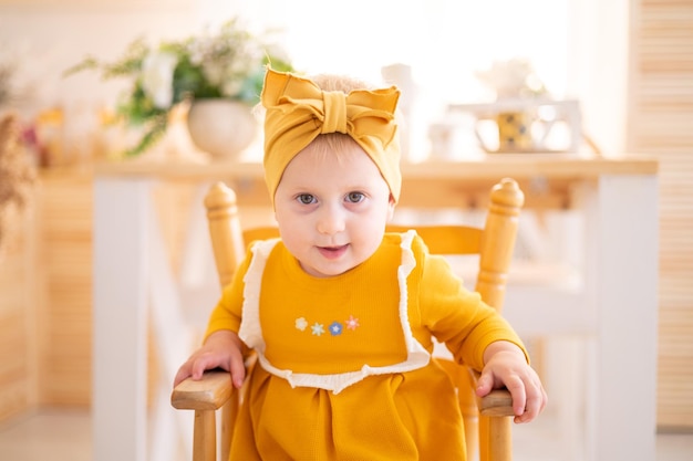 Ragazza in buona salute sveglia in vestito di cotone giallo che si siede su un seggiolone nella cucina della casa che alimenta i bambini cibo per bambini