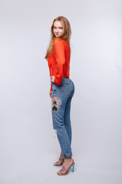 Ragazza in camicetta rossa e jeans in posa sulla parete isolata