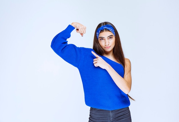 Ragazza in camicia blu che mostra i suoi muscoli del braccio.