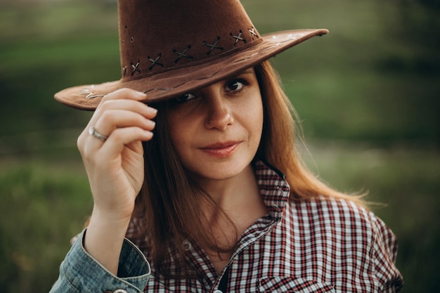 Ragazza in camicia in stile country americano e cappello da cowboy in natura sul tramonto