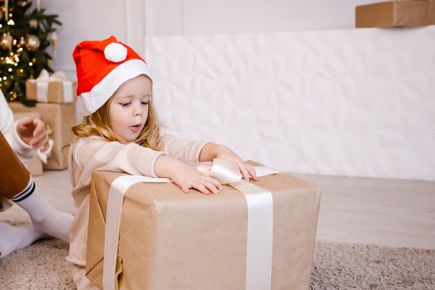 Ragazza in cappello della Santa con il regalo di Natale sulla priorità bassa dell'albero di Natale.