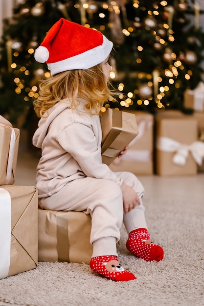 Ragazza in cappello della Santa con il regalo di Natale sulla priorità bassa dell'albero di Natale.