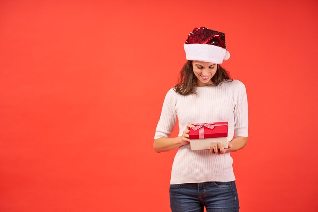 Ragazza in cappello di babbo natale con regalo di natale sorridente su sfondo arancione