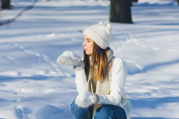 Ragazza in cappello e guanti che soffia neve