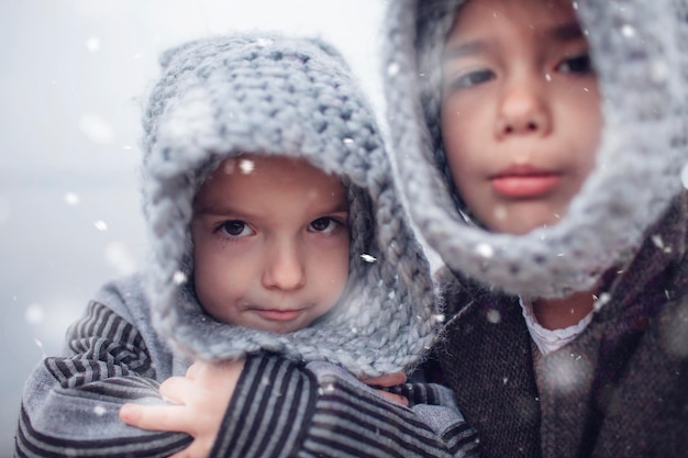 Ragazza in cappello grigio tricottato che abbraccia suo fratello minore congelato