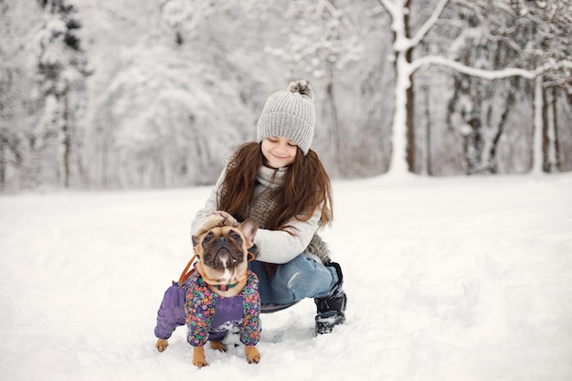 Ragazza in cappello lavorato a maglia che gioca con il suo cane bulldog francese su una neve