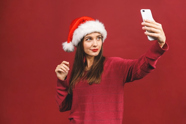 Ragazza in costume da Babbo Natale sorridente e tenendo selfie sul cellulare