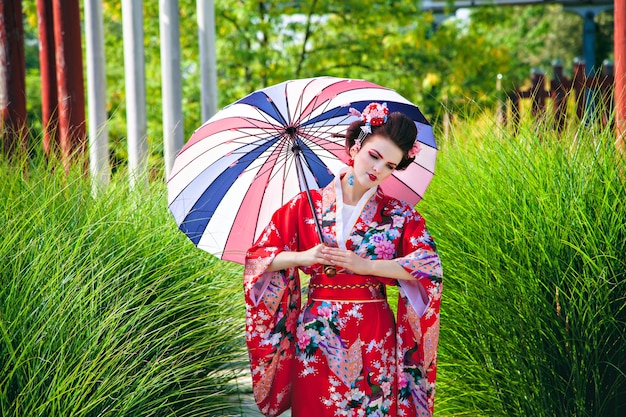 Ragazza in costume da geisha con trucco fantasia in giardino con ombrellone