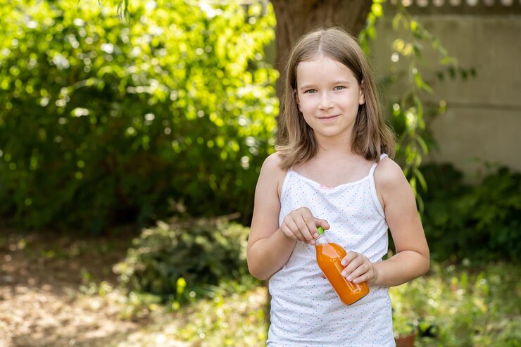 Ragazza in età scolastica elementare che tiene in mano una bottiglia di vetro piena di succo d'arancia naturale sano e sorridente