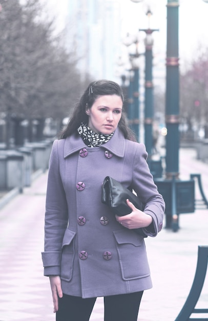 Ragazza in fioletovo cappotto autunnale con borsa al parco