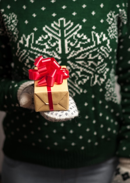 Ragazza in guanti e un maglione con un ornamento invernale detiene i regali di Natale