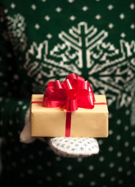 Ragazza in guanti e un maglione con un ornamento invernale detiene i regali di Natale