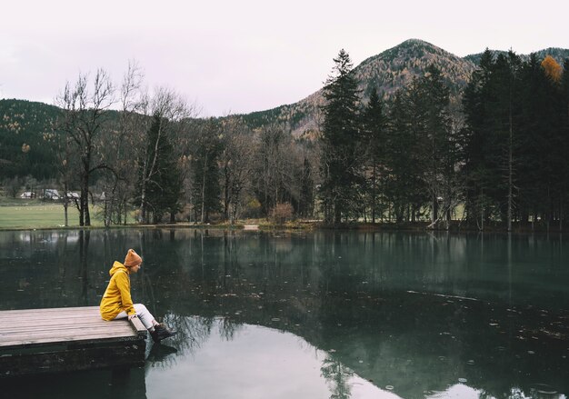 Ragazza in impermeabile giallo guardando il lago di montagna in Jezersko Adventure travel in Slovenia