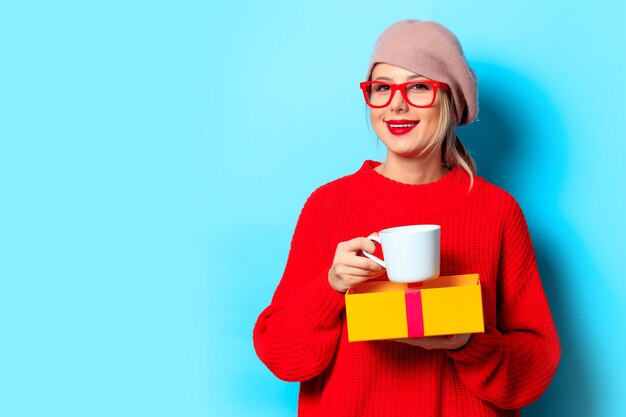 Ragazza in maglione rosso con confezione regalo e tazza di caffè