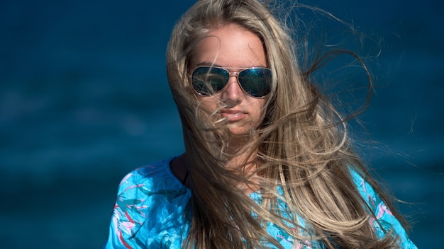 Ragazza in occhiali da sole con capelli lunghi sulla a del mare blu.