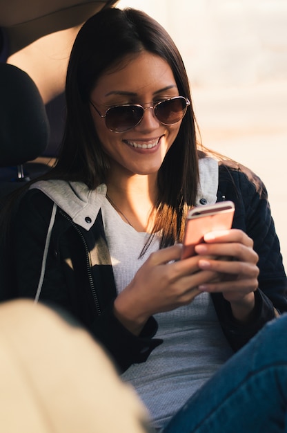 Ragazza in occhiali da sole sorridente e leggendo un messaggio in macchina