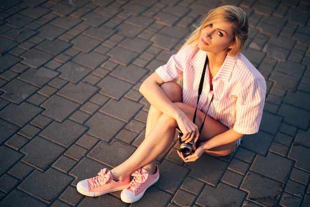 ragazza in pantaloncini con la macchina fotografica che riposa e si siede a terra