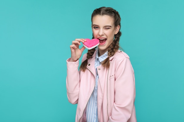 Ragazza in piedi e tenendo la forma di cuore rosa e guardando la telecamera e cercando di mordere