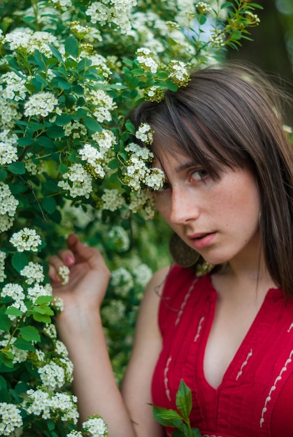 Ragazza in piedi vicino a un cespuglio verde con fiori bianchi in fiore