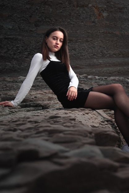 Ragazza in posa con un abito bianco e nero in una baia rocciosa della costa basca.