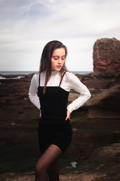 Ragazza in posa con un abito bianco e nero in una baia rocciosa della costa basca.