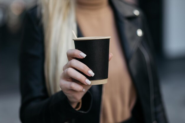 Ragazza in possesso di una tazza di cartone Tazza di caffè di carta in una mano di donna sullo sfondo del negozio Bevanda calda Mano che tiene tazza di caffè di carta Tazza di caffè di carta