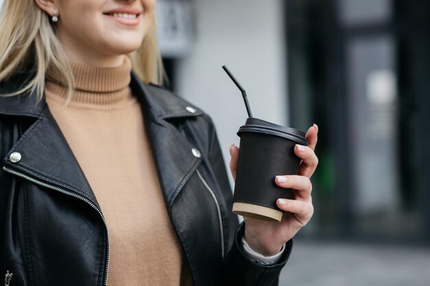 Ragazza in possesso di una tazza di cartone Tazza di caffè di carta in una mano di donna sullo sfondo del negozio Bevanda calda Mano che tiene tazza di caffè di carta Tazza di caffè di carta