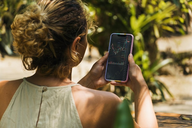 Ragazza in possesso di uno smartphone con grafico del mercato azionario finanziario sullo schermo nel parco. Borsa valori.